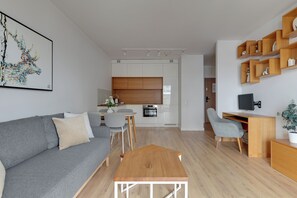 Una sala de estar moderna con un sofá gris, una mesa de centro de madera y un comedor con una mesa y sillas blancas.