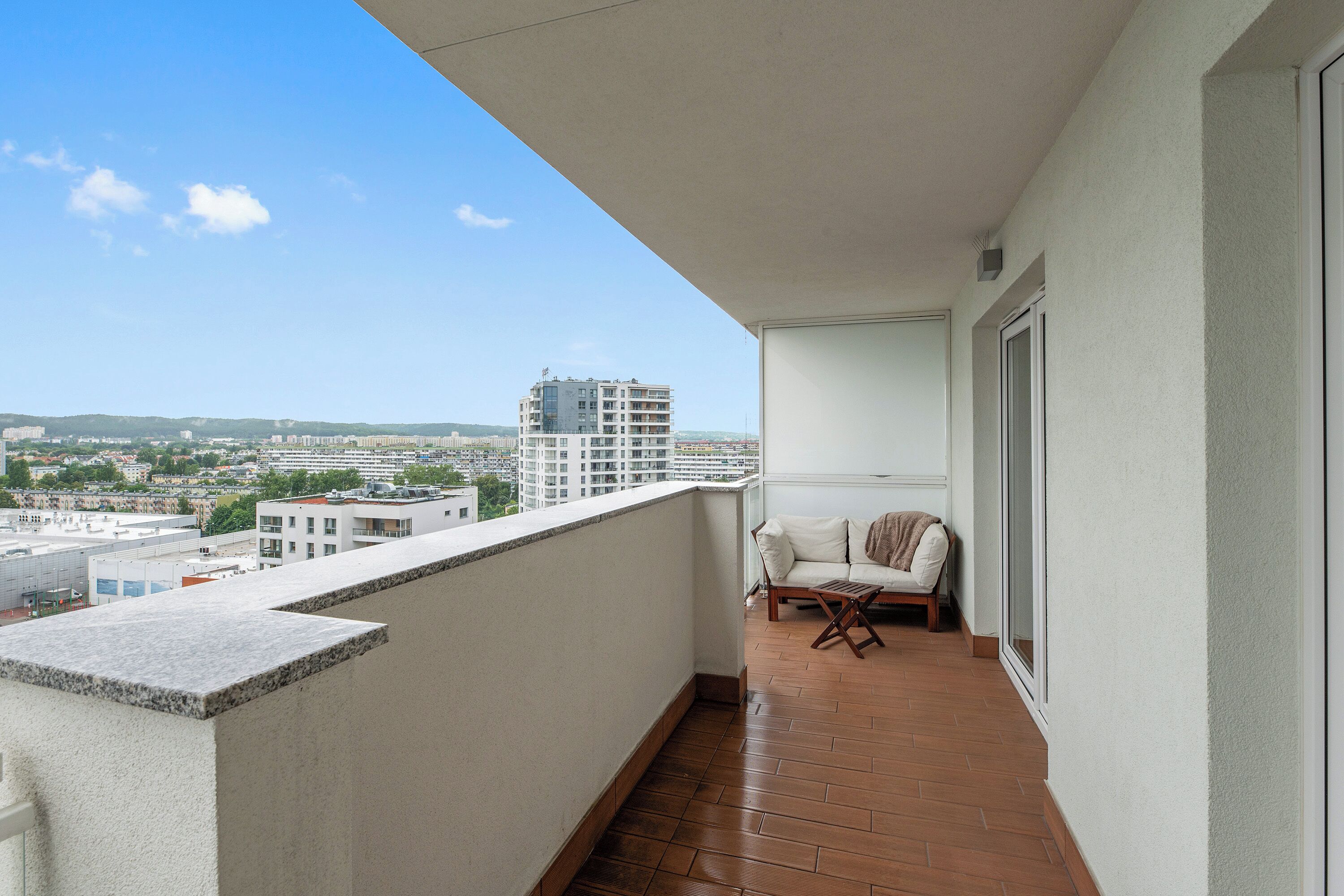 Ein Balkon mit Blick auf eine Stadtansicht, ein weißes Sofa und ein Holztisch.