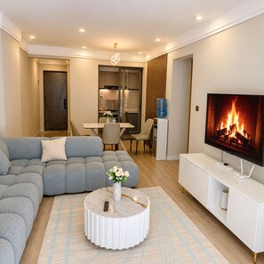 Una sala moderna con un sofá modular, una mesa de centro redonda, un televisor de pantalla plana y un comedor con una mesa y sillas.