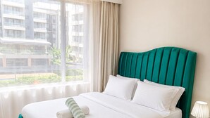 A hotel room with a bed, a nightstand, a lamp, a window with curtains, and a view of buildings outside.