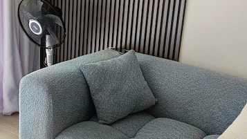 A sectional sofa with a textured fabric, a standing fan, and a vertical slatted wall in the background.