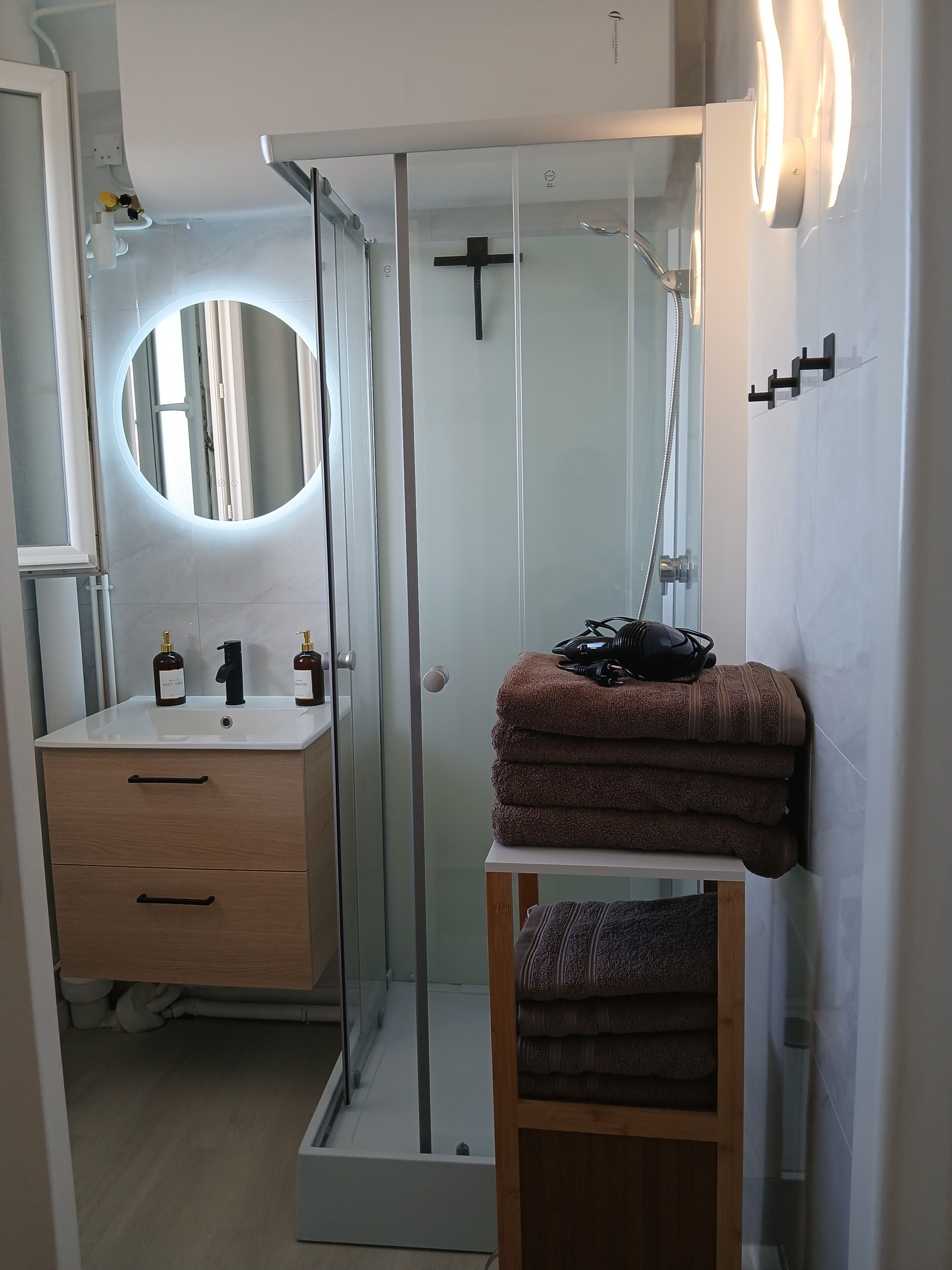 Un baño moderno con cabina de ducha de vidrio, tocador con espejo y perchero.