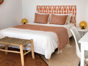 Ein ordentlich eingerichtetes Schlafzimmer mit Bett, Nachttischen, einer Bank und einem gemusterten Teppich.