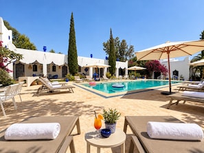 A poolside area with lounge chairs, a pool, and a building with white walls and blue accents. - Palais Mogaya (Essaouira)