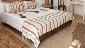 Ein Schlafzimmer mit einem hölzernen Bett, gestreifter Bettwäsche, einem kleinen Holzstuhl, einem runden Spiegel und einem gewebten Teppich.