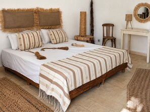 Ein Schlafzimmer mit einem hölzernen Bett, gestreifter Bettwäsche, einem kleinen Holzstuhl, einem runden Spiegel und einem gewebten Teppich.