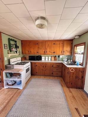 A kitchen with wooden cabinets, a gas stove, a sink, and a window with plants. - High Noon Cottage! A charming 3BR cottage at North Beach! (Hampton)