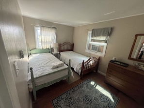Ein Schlafzimmer mit zwei Einzelbetten, einem Schminktisch, einem Fenster mit Vorhängen und einem gemusterten Teppich.
