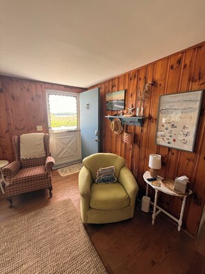 A cozy room with a plaid armchair, a green armchair, a small table with a lamp, and a wall decorated with maritime-themed artwork. - High Noon Cottage! A charming 3BR cottage at North Beach! (Hampton)