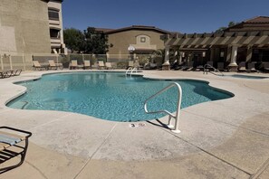 A swimming pool with a diving board, lounge chairs, and a building in the background.