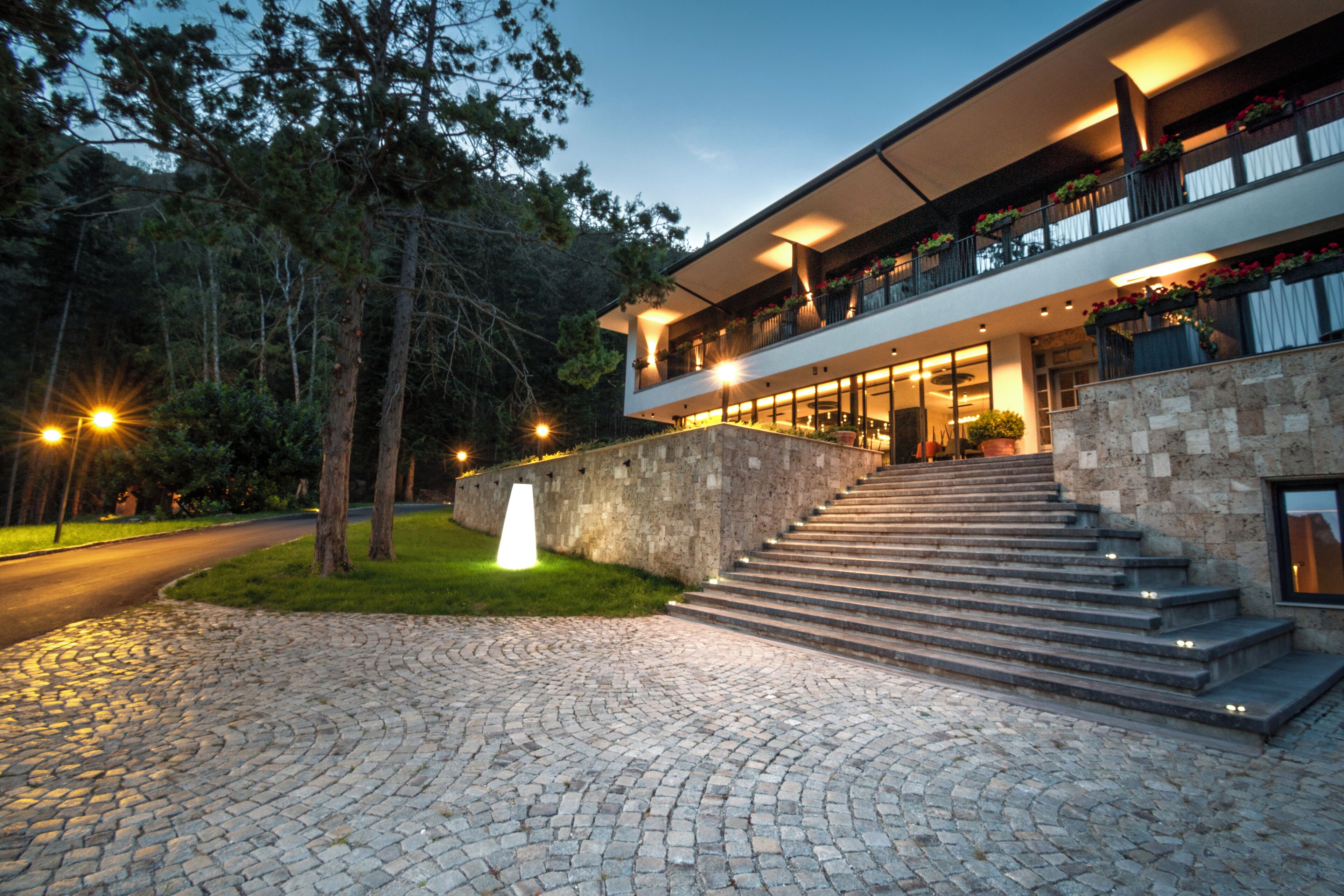 A modern building with a stone facade, a staircase leading to a balcony, and a well-lit entrance.