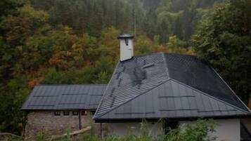 A house with a sloped roof, surrounded by dense forest and mountains.