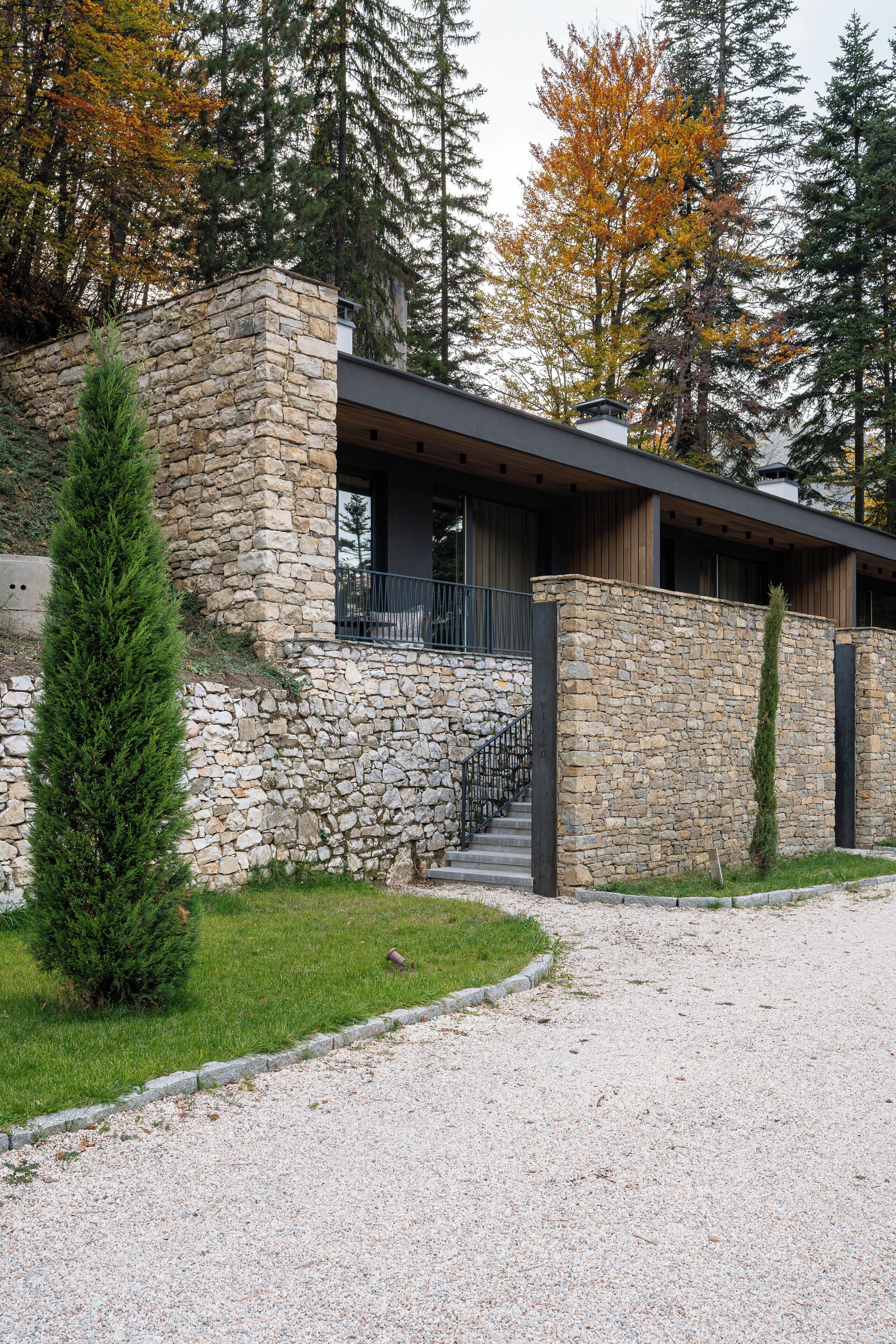 Un edificio moderno con fachada de piedra, terraza de madera y camino de entrada de grava.