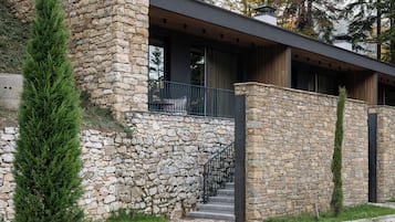 Un edificio moderno con fachada de piedra, terraza de madera y camino de entrada de grava.