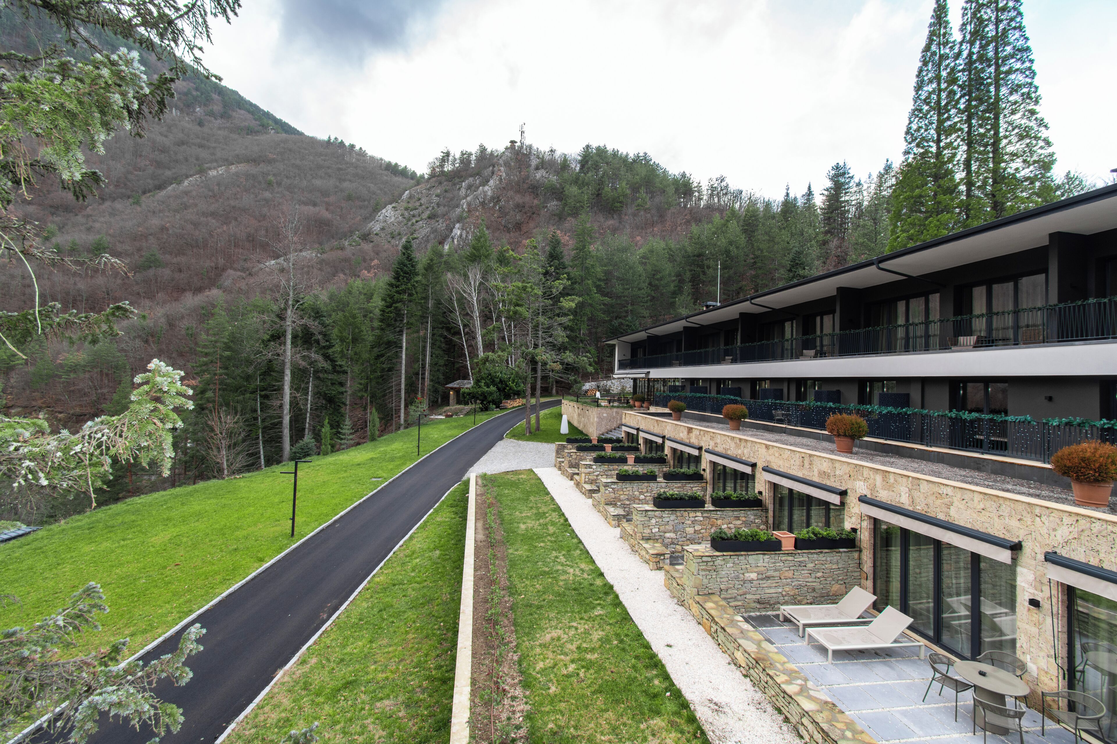 Un hotel con un largo pasillo, mobiliario exterior y montañas al fondo.