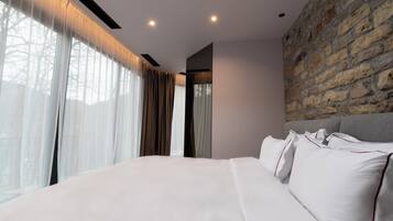A modern bedroom with a large bed, a stone accent wall, and sheer curtains.