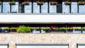 Un edificio moderno con fachada de piedra, un balcón con jardineras de flores y una puerta de vidrio que da a una zona de estar al aire libre.