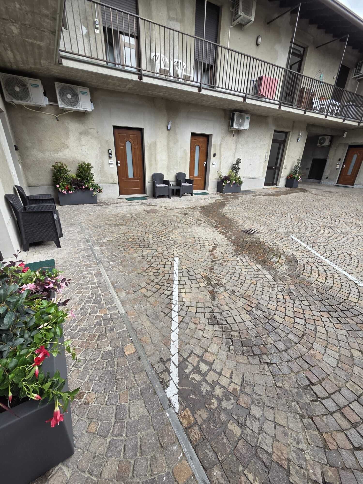 A courtyard with a cobblestone floor, outdoor seating, and a building with multiple doors and windows.
