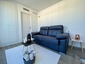 Ein modernes Wohnzimmer mit einem dunkelblauen Sofa, einem kleinen Tisch mit Kerzen und einer Lampe auf einem Beistelltisch.