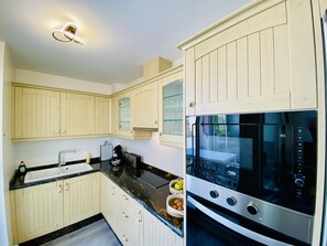 Eine moderne Küche mit hellen Holzschränken, einer schwarzen Arbeitsplatte, einem eingebauten Ofen und einem gläsernen Schrank mit Weingläsern.