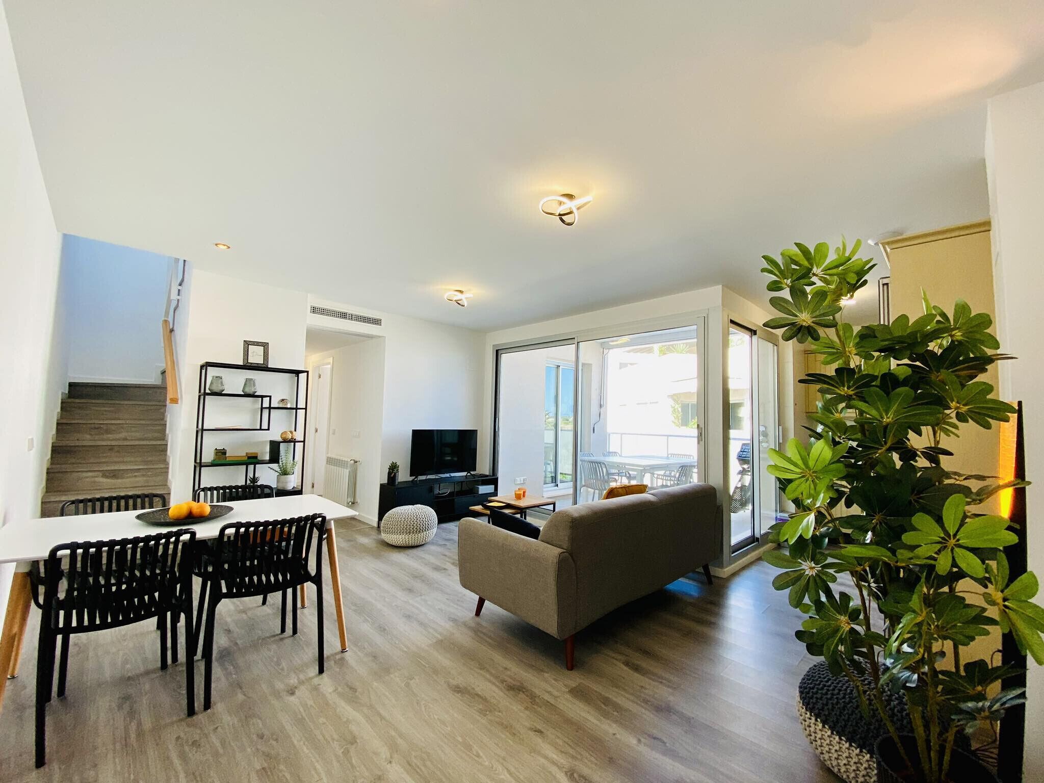 A modern living room with a sofa, dining table, chairs, and a TV.