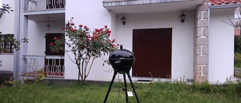 A black barbecue grill on a grassy lawn in front of a building with a balcony and a red door.