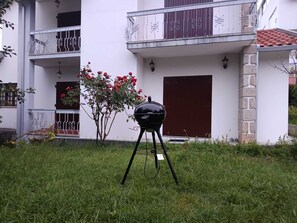 A black barbecue grill on a grassy lawn in front of a building with a balcony and a red door. - Discover the perfect getaway in the heart of Vouzela and feel the rhythm of nature! (Vouzela)