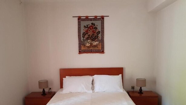 A neatly made bed with white linens and towels, two bedside tables with lamps, and a decorative tapestry on the wall. - Discover the perfect getaway in the heart of Vouzela and feel the rhythm of nature! (Vouzela)