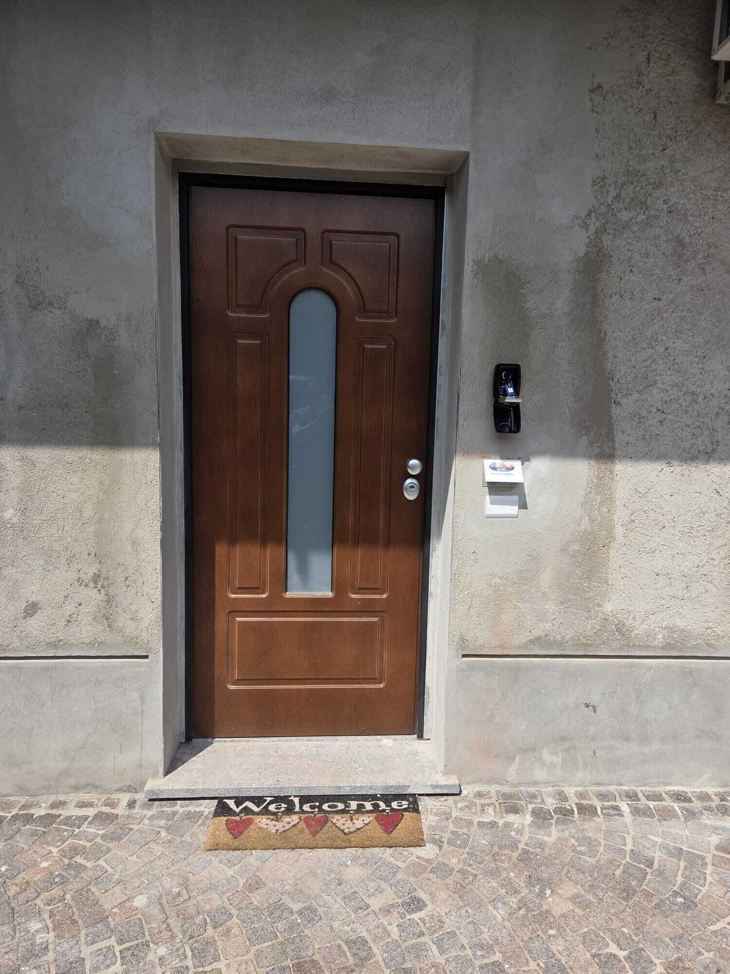 Una porta marrone con un pannello di vetro, una fessura per la posta e un tappetino d'ingresso con la scritta 'Welcome'.