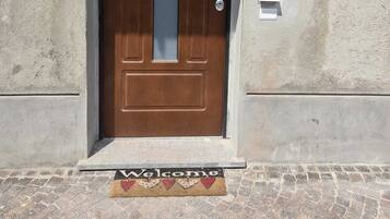 Una porta marrone con un pannello di vetro, una fessura per la posta e un tappetino d'ingresso con la scritta 'Welcome'.