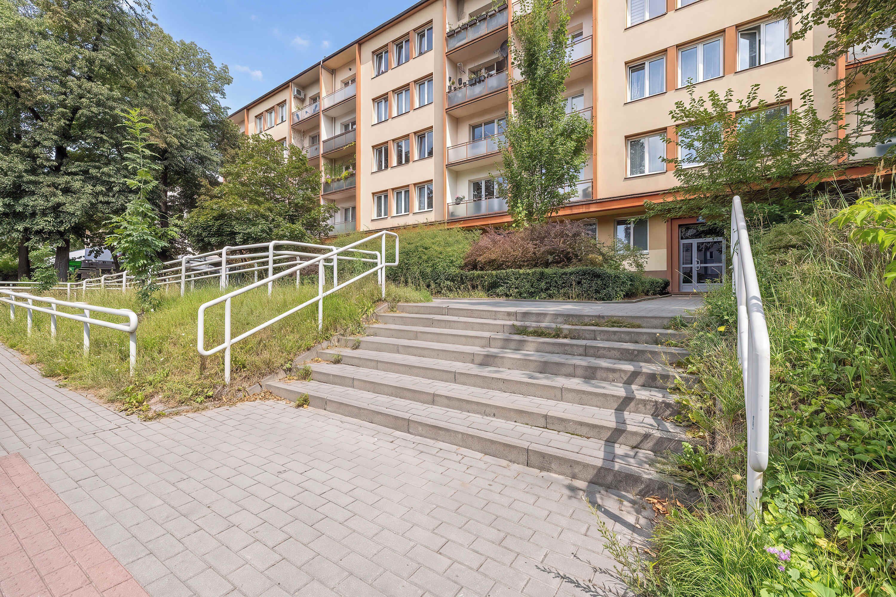 Un immeuble résidentiel à plusieurs étages, avec un escalier menant à l’entrée.