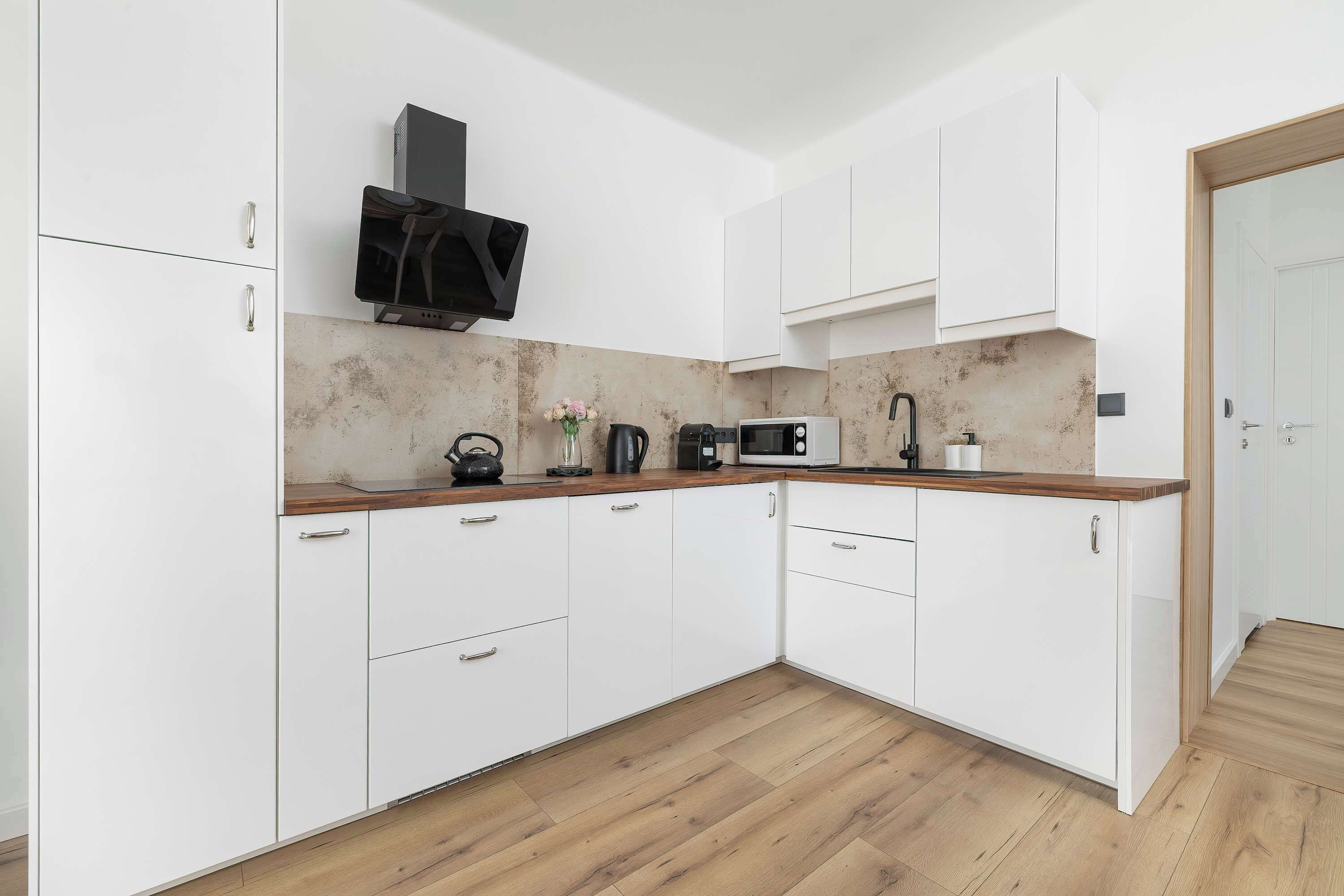 Une cuisine moderne avec des meubles blancs, un plan de travail en bois et un four à micro-ondes.