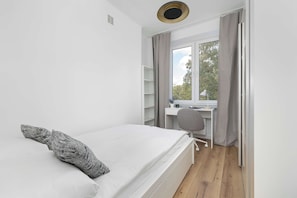 Ein schlicht eingerichtetes Schlafzimmer mit Bett, Schreibtisch und einem Fenster mit Vorhängen.