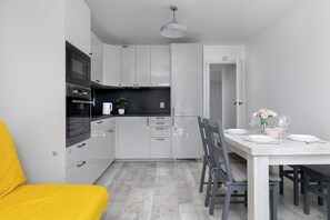 A modern kitchen with white cabinetry, a black microwave, and a dining area with a white table set for two. - Spacious Apartment with Balcony and Desk | Bathtub (Kraków)