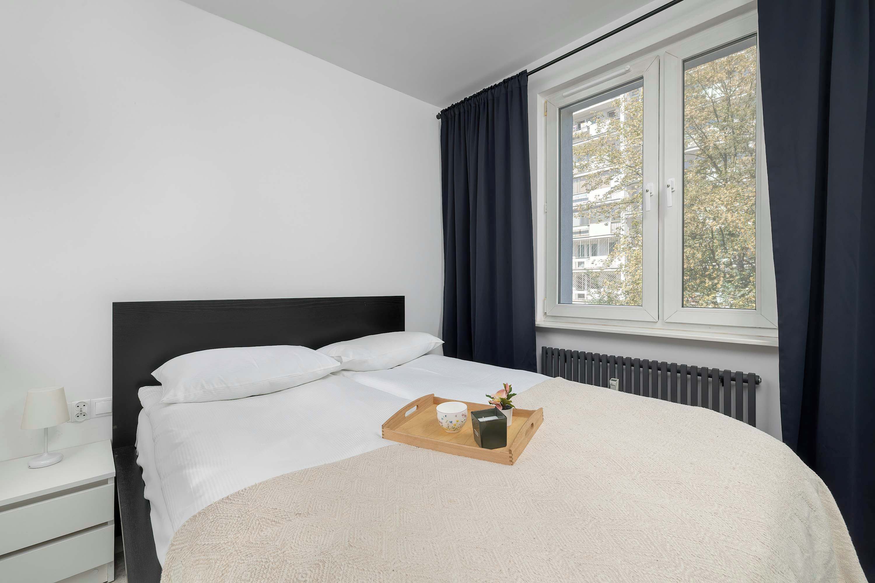 Een slaapkamer met een bed, nachtkastje, raam met gordijnen en een radiator.