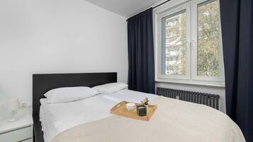 Een slaapkamer met een bed, nachtkastje, raam met gordijnen en een radiator.