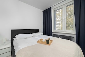 A bedroom with a bed, a nightstand, a window with curtains, and a radiator. - Spacious Apartment with Balcony and Desk | Bathtub (Kraków)