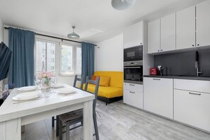 A modern kitchen with white cabinets, a yellow sofa, and a dining table set for two. - Spacious Apartment with Balcony and Desk | Bathtub (Kraków)