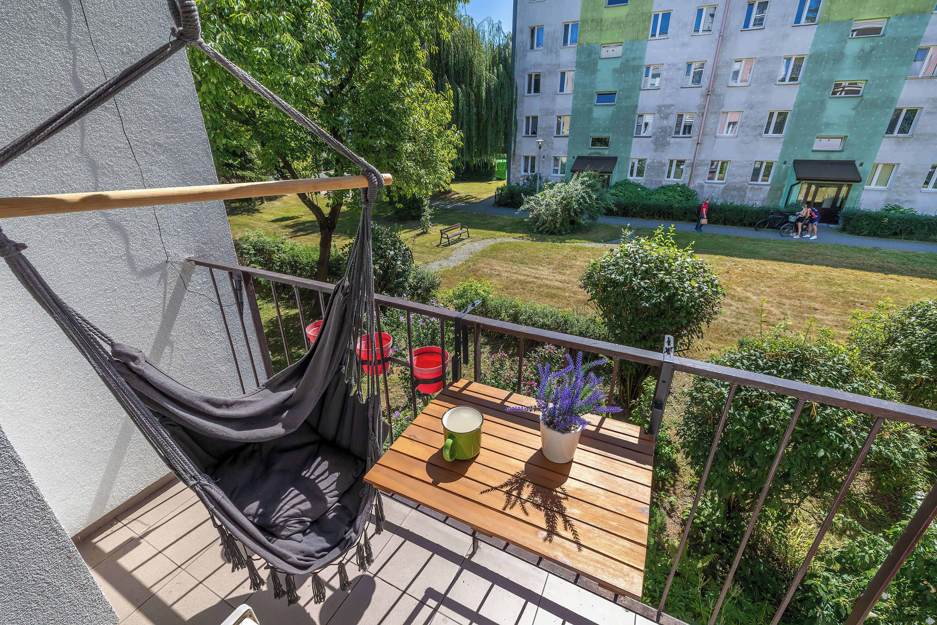 Een balkon met een hangmat, een houten tafel en een bloempot.