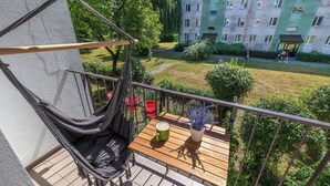 Parvekkeella on riippukeinu, puinen pöytä ja ruukussa oleva kasvi.