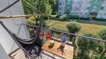 Een balkon met een hangmat, een houten tafel en een bloempot.