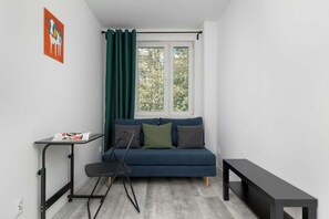 Ein kleiner, moderner Raum mit einem blauen Sofa, einem Stehpult und einem Fenster mit Vorhängen.