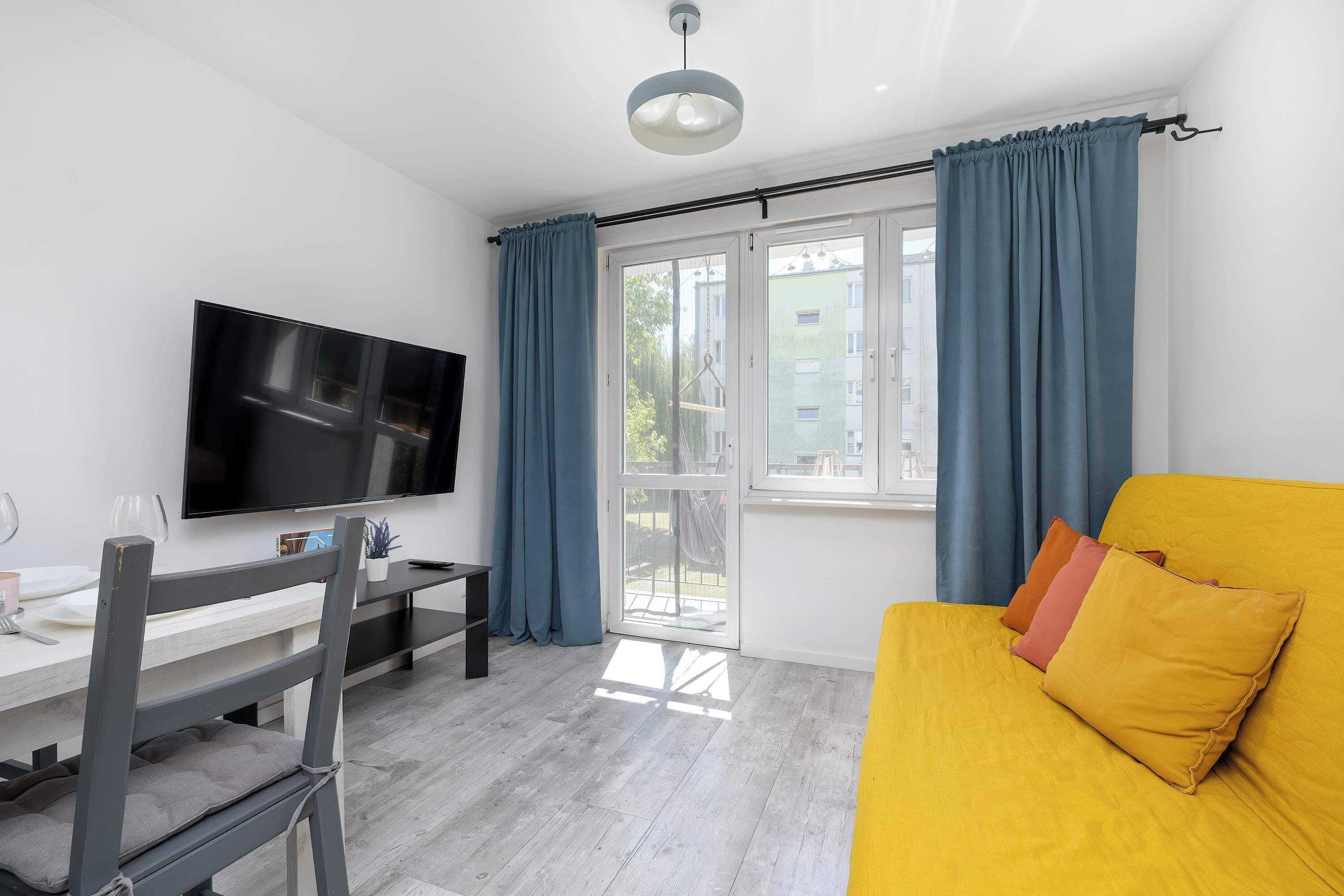 Een moderne woonkamer met een flatscreen televisie, een eettafel en een bank met kussens.