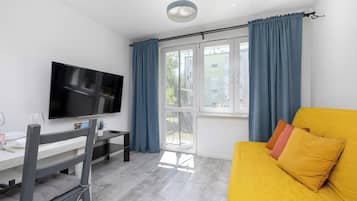 Een moderne woonkamer met een flatscreen televisie, een eettafel en een bank met kussens.