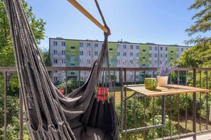 A hammock chair on a balcony with a view of a multi-story building and greenery. - Spacious Apartment with Balcony and Desk | Bathtub (Kraków)