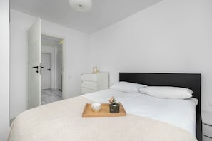 A modern bedroom with a bed, a bedside table, a dresser, and a door leading to another room. - Spacious Apartment with Balcony and Desk | Bathtub (Kraków)