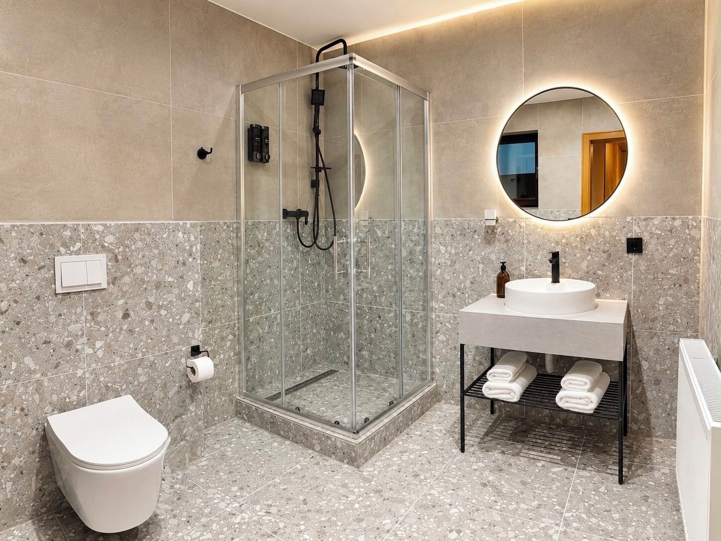 A modern bathroom with a glass-enclosed shower, a round mirror, a white sink, and a toilet.