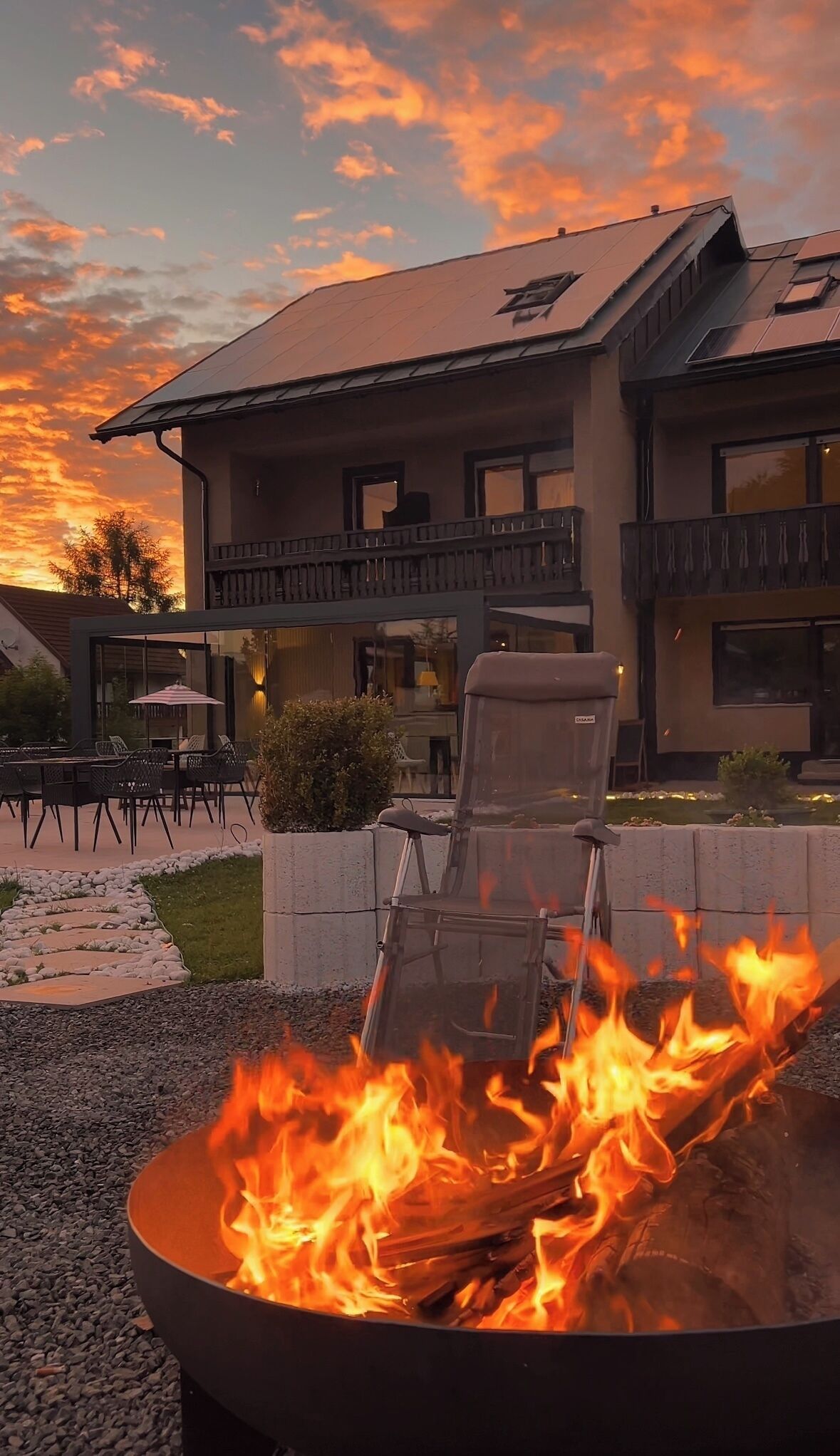 A fire pit with flames in front of a building with a balcony and outdoor seating.