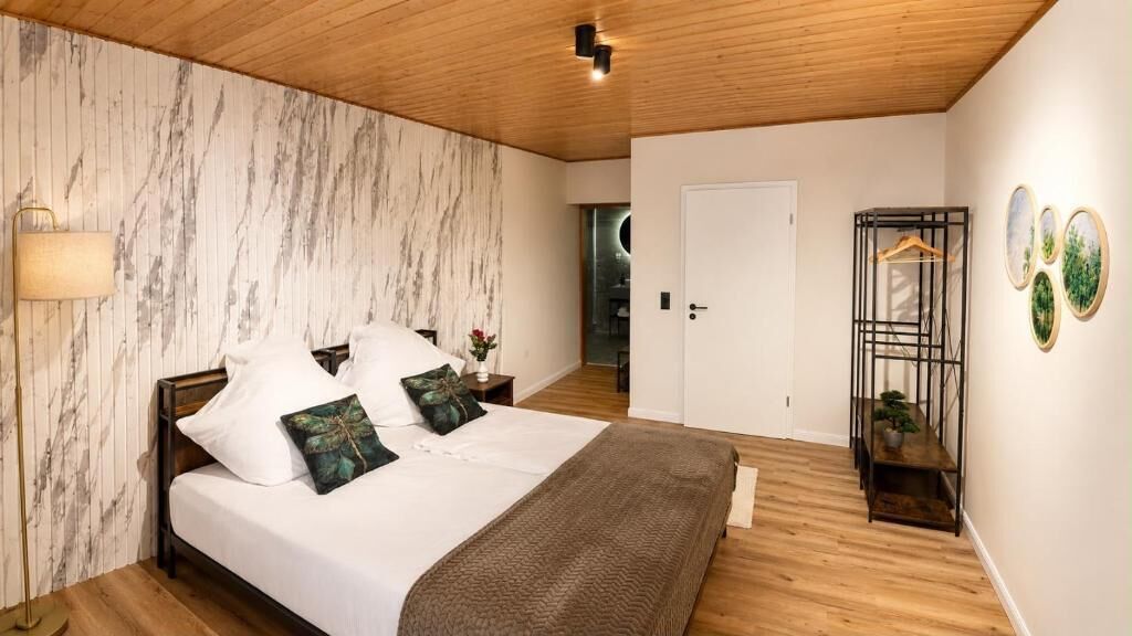 A bedroom with a bed, bedside tables, a lamp, a door, and a wall-mounted shelf with a plant.