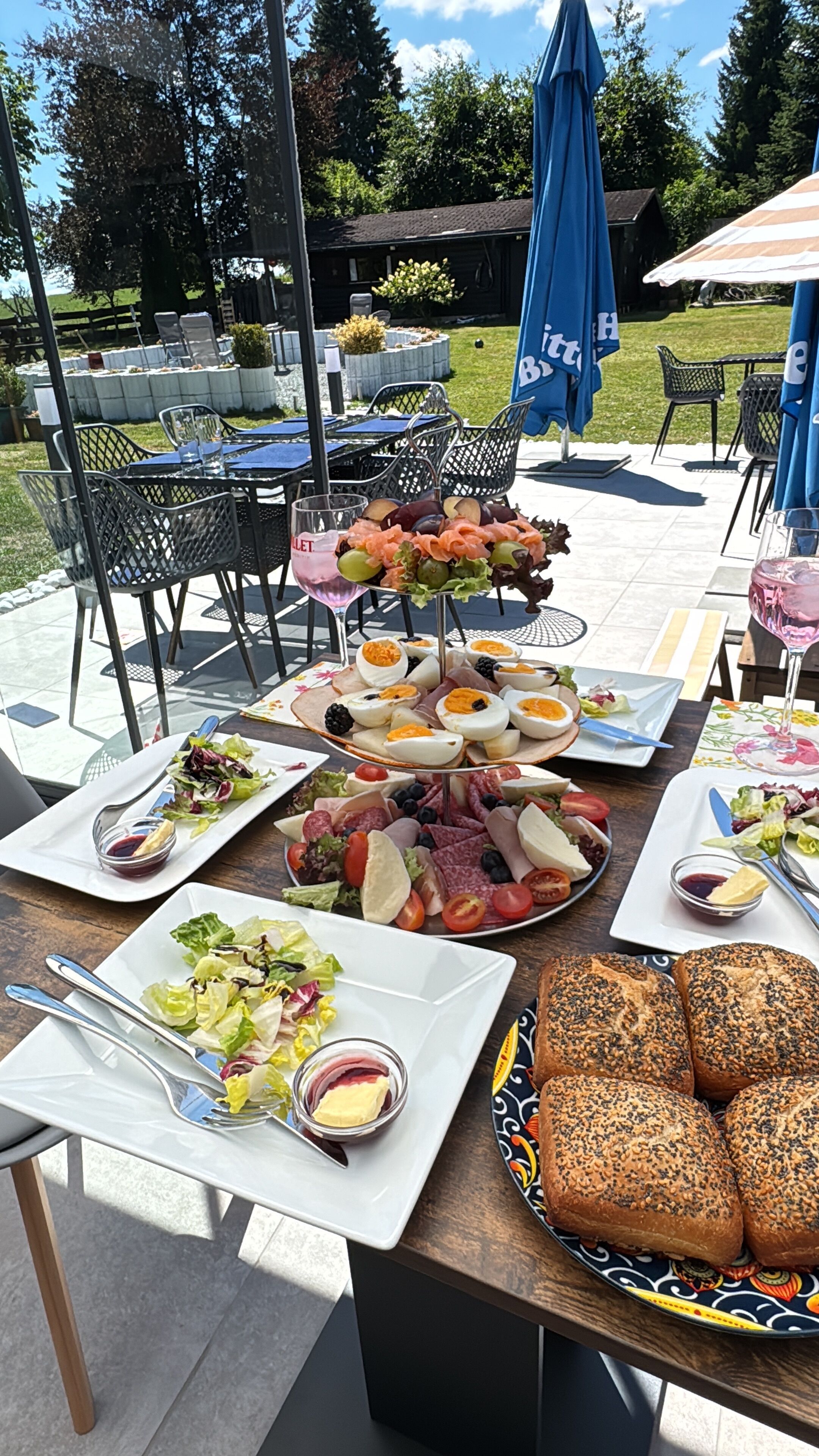 An outdoor dining area with tables set for meals, including a variety of food platters and bread.